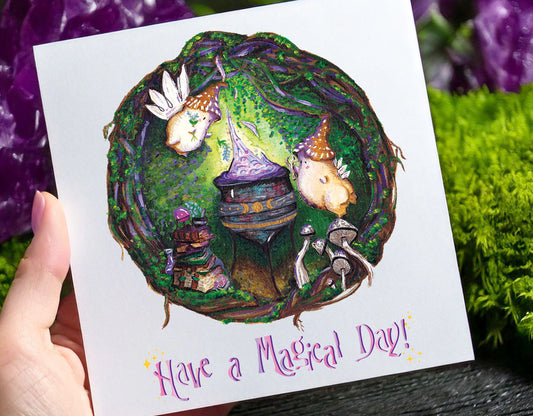 a white square greetings card featuring an image of two witch mushroom fairies adding plants to a bubbling cauldron in a forest. they are surrounded by green trees, moss, bushes and vines. beside them is a pile of books, crystal ball, crystals, pessel and mortar and mushrooms
the text reads 'have a magical day'