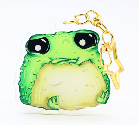 Grumpy green toad keychain with a gold star clip on a white background