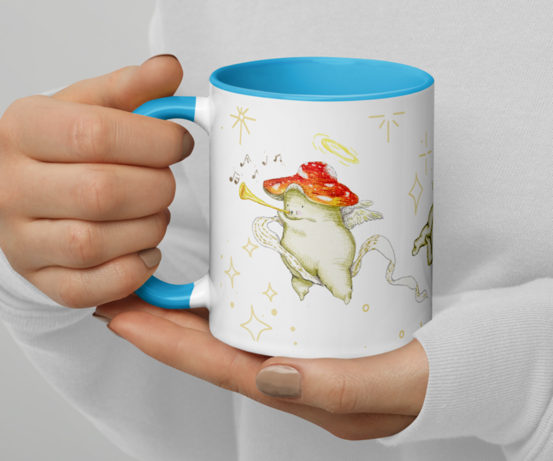 image shows a white ceramic mug which is blue on the uinside, and the handle. The design features illustrations of cherub mushrooms playing instruments and flying amongst a starry backdrop. The mug is being held by the two hands of a person wearing a white top