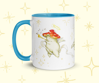 image shows a white ceramic mug which is blue on the uinside, and the handle. The design features illustrations of cherub mushrooms playing instruments and flying amongst a starry backdrop. The mug is imposed in front of a cream background with star graphic details