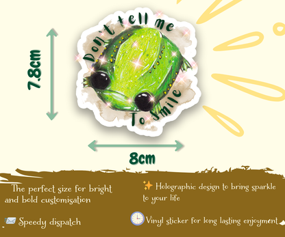 image shows product descriptions for a vinyl sticker featuring an illustration of Glumbert the Sad Toad, Around his body is a brown watercolour smugde and the words, "Dont tell me to smile". Arrows show measurements of the sticker, 7.8cm x 8cm, and at the bottom of the image words read, perfect size for bright and bold customisation, speedy dispatch, holographic design to bring sparkle to your life, vinyl sticker for long lasting enjoyment