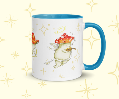 image shows a white ceramic mug which is blue on the uinside, and the handle. The design features illustrations of cherub mushrooms playing instruments and flying amongst a starry backdrop. The mug is imposed in front of a cream background with star graphic details