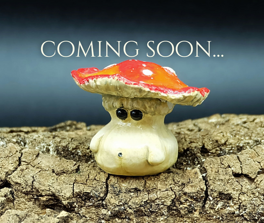 A handcrafted miniature sculpture of a fly agaric toadstool mushroom character with a subdued expression. Sculpture is photographed upon a piece of tree bark