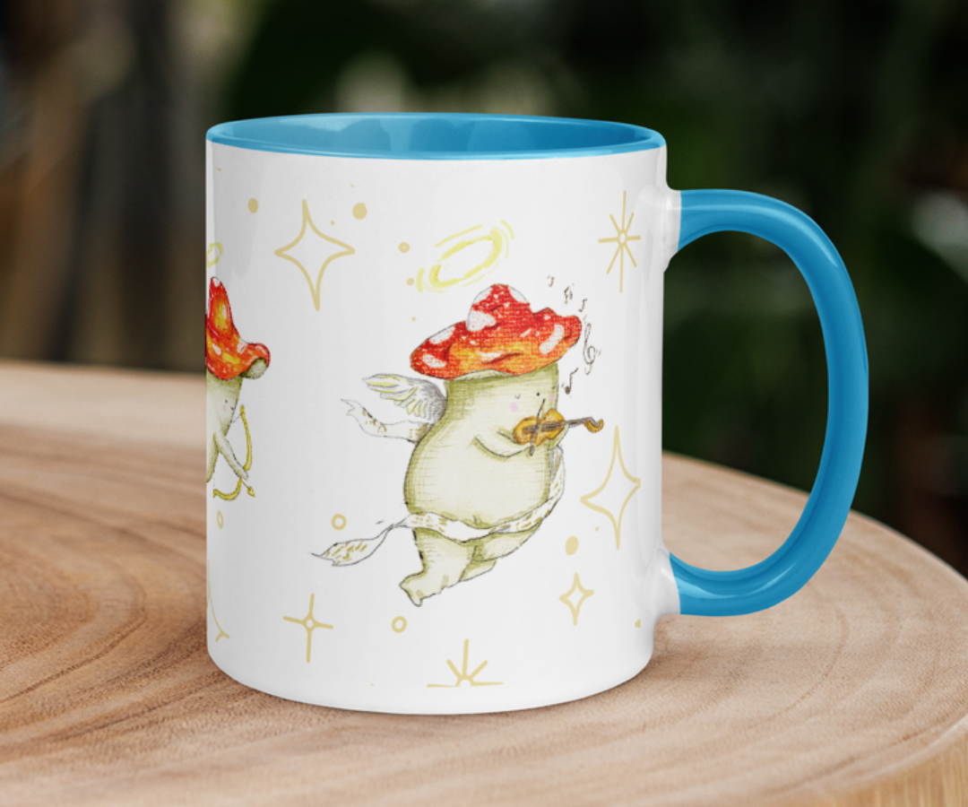 image shows a white ceramic mug which is blue on the uinside, and the handle. The design features illustrations of cherub mushrooms playing instruments and flying amongst a starry backdrop. The mug is placed on top of a wooden log slice with blurred impressions of trees in the background