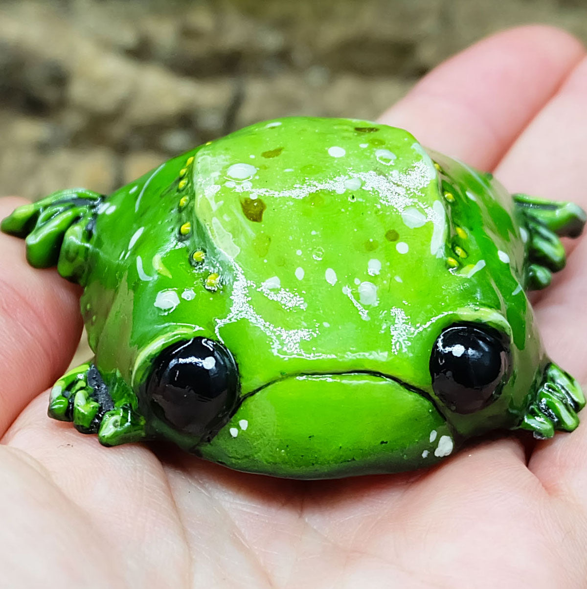 a sculpture of a sad toad sits in soeones hands. its a collectible figurine of a sad frog