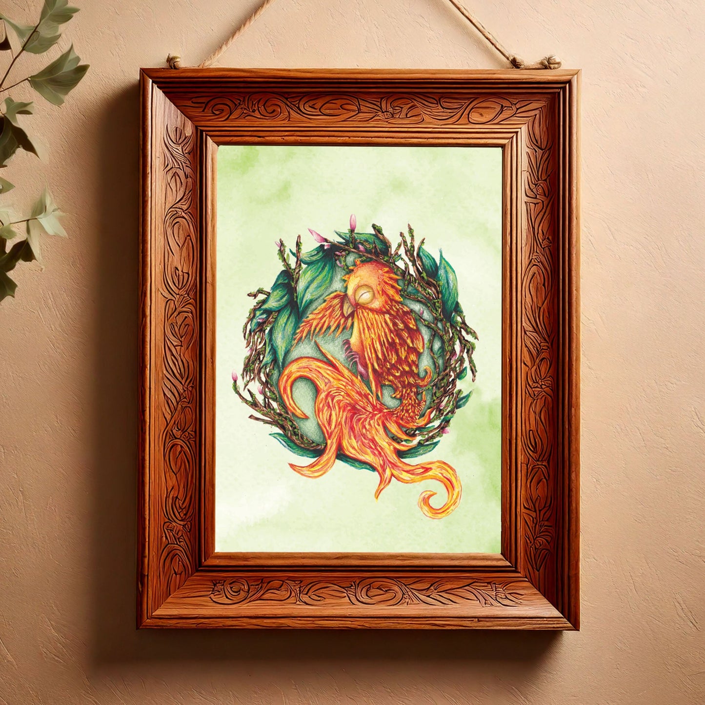 image shows a portrait art print featuring a painting of a baby phoenix resting on it's side, inside a nest made of twigs, leaves and budding flowers. behind the main detail of the painting, there is a green watercolour wash making the background mottled green. it is placed inside a carved wooden frame  which is hanging against a light terracotta venetian plaster wall, and to the left the leaves of a plant creep into the corner of the frame 