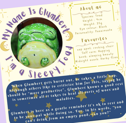 image shows a close up of sleepy glumberts backstory card, which is included in the rest and recovery mental health box, the totle reads 'my name is glumbert, I'm a sleepy toad'. This text goes around a photograph of glumbert sleeping . The additional text describes some 'about me' facts and favourites. at the bottom of the card, there is a short paragraph explaining a little more about glumbert the sleepy toad