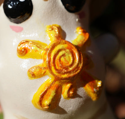 a n extreme close up of Alba's sunshine which is placed on her belly. the image shows the metallic gold details and highlights of her yellow and orange sun