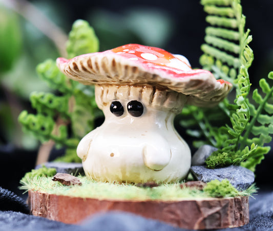 Adorable fly agaric mushroom figurine with a colorful red cap placed on a wooden basesurrounded by a diorama of plants