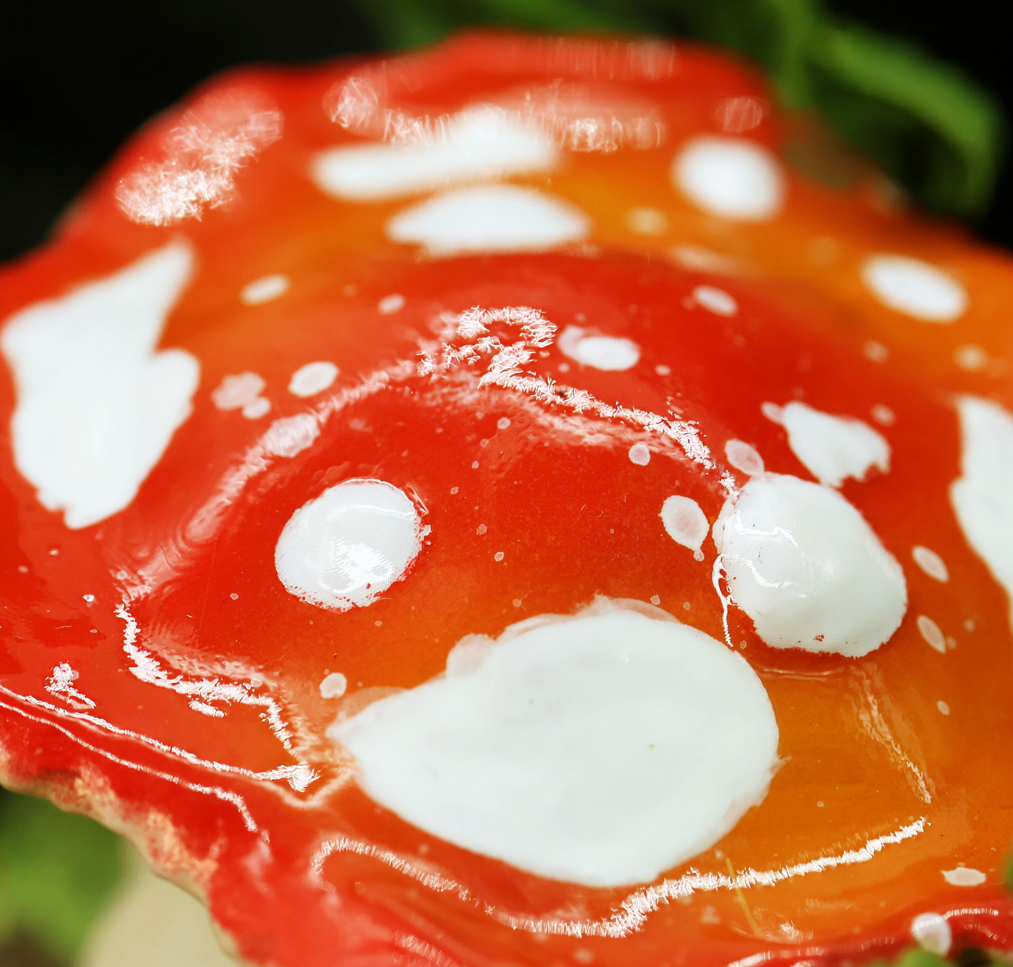 Close-up of the sculptures shiny red mushroom cap with white spots against a dark background 