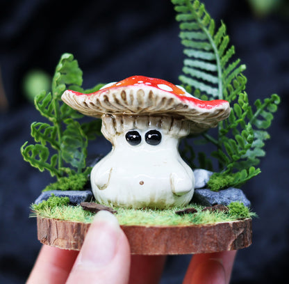 Small mushroom figurine with a red cap held between fingers against a dark background