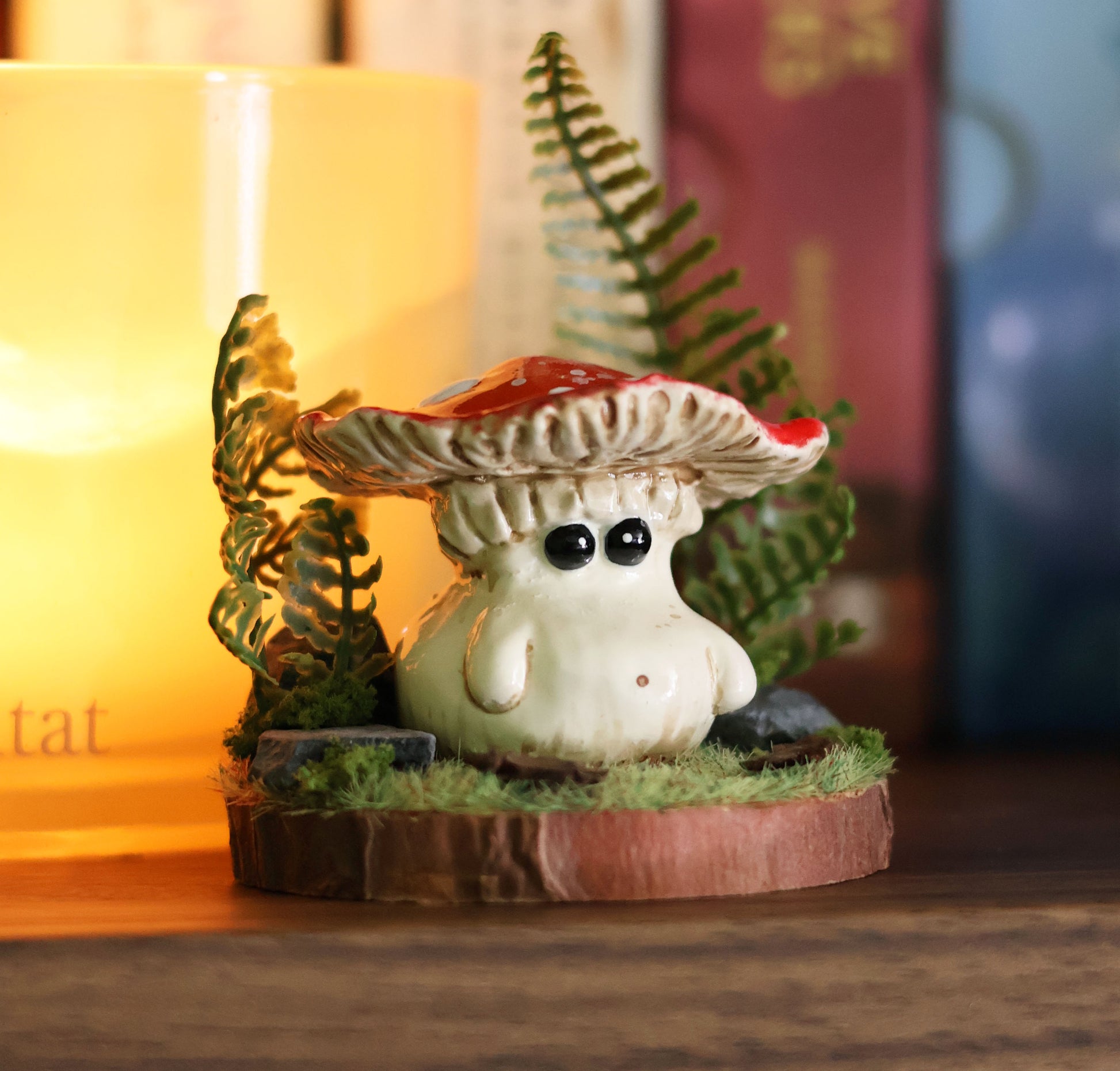 Small figurine of a mushroom with a red cap on a wooden base, surrounded by greenery.