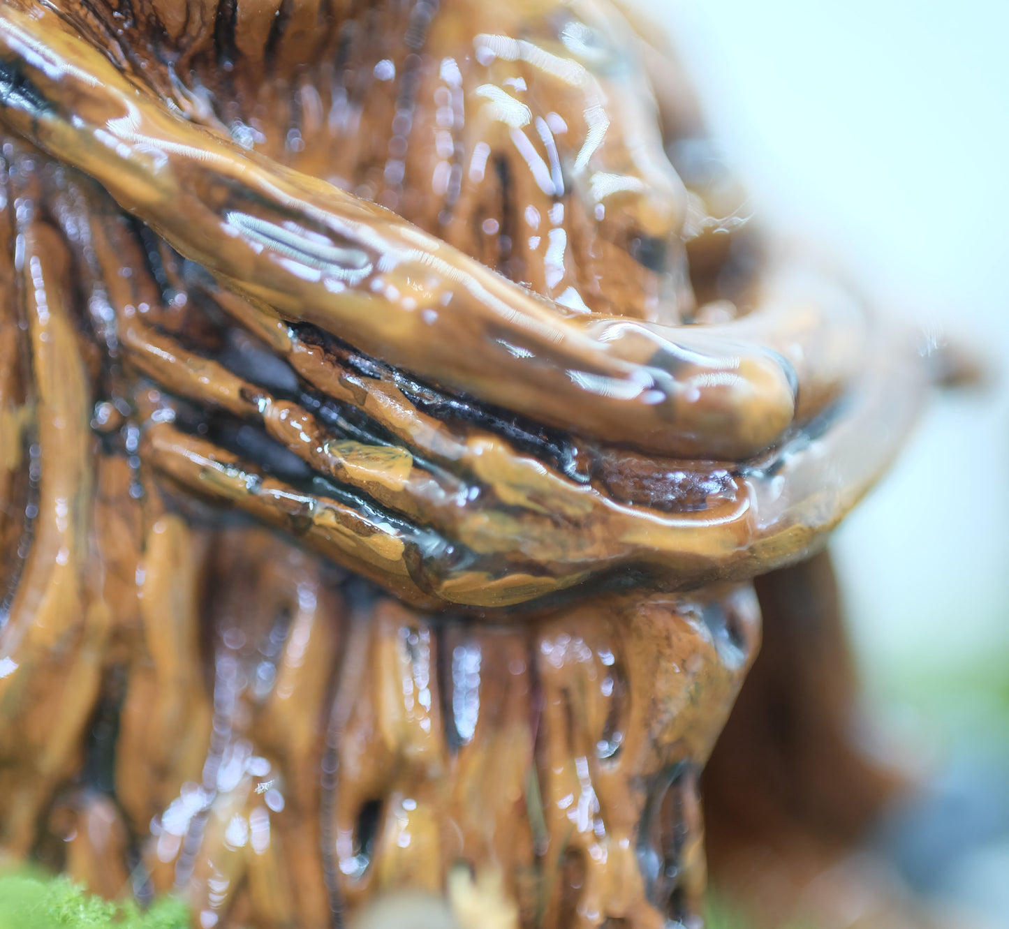 This photo shows a close up of the sculpture. Splint is hugging their legs close to their body. The photograph shows the intricate details of the sculpting work, texture and colours. The sculpture is shown against a white background