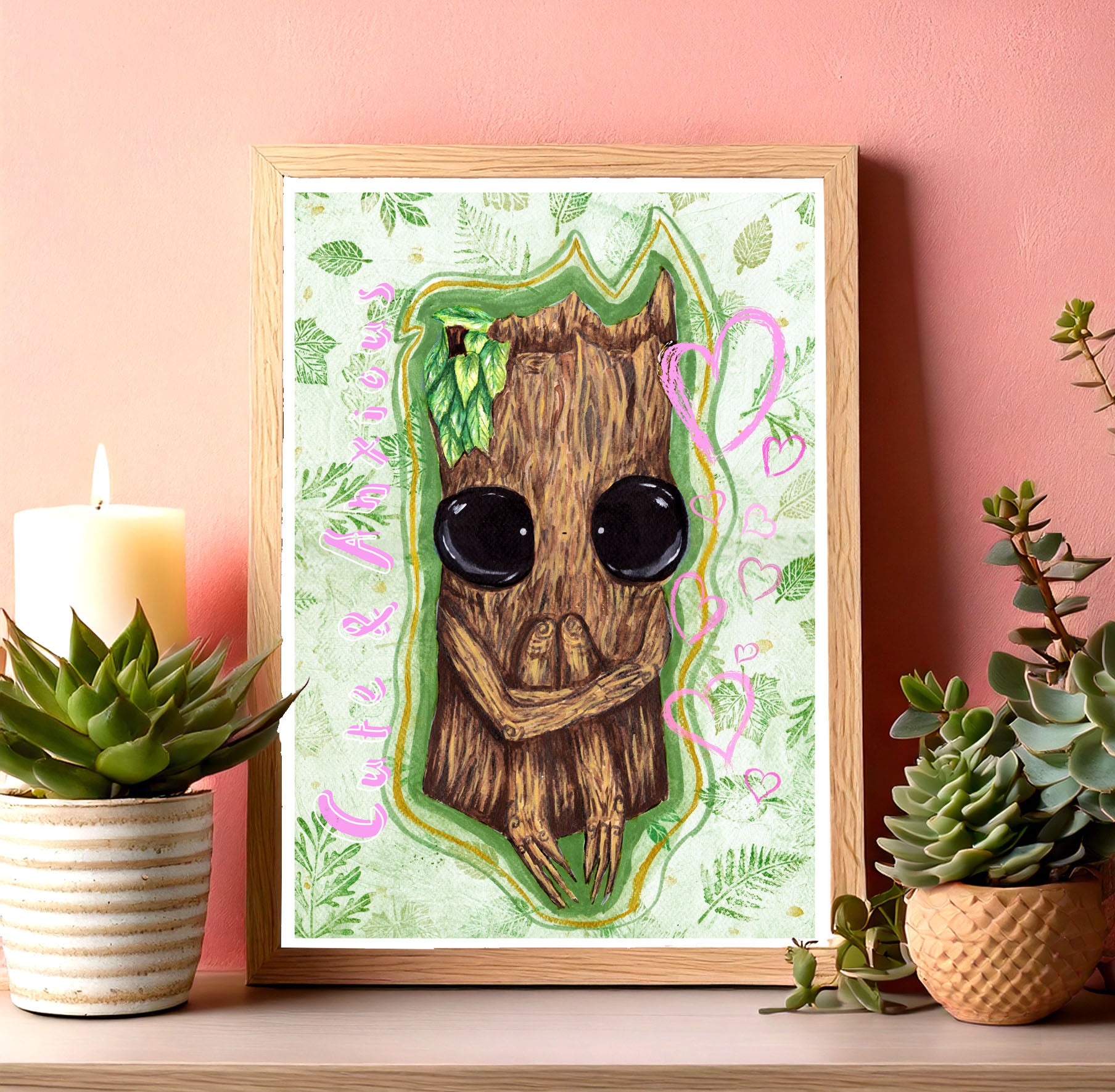 Art print in wooden frame with plants & a candle, all photographed against a pink wall. The art print features cute & anxious Splint the Twigling, a wooden fantasy creature who is hugging their knees in a seated position. They have big black eyes & are painted onto a green background with green leaves surrounding them. Pink words read, 'Cute and Anxious' to the left of Splint, & to the right of them are a selection of pink hearts in various sizes. Splint is surrounded by a green & golden glow