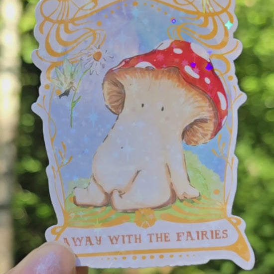 a holographic vinyl sticker with away with the fairies written on it underneath artwork of a toadstool mushroom meeting a fairy who is offering it a daisy