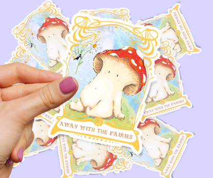 Image shows sticker of toadstool mushroom seated on a bed of mossy grass, they are looking up at a fairy who is handing them a daisy from above. The artwork is framed by an ornate gold art nouveau style frame. the sticker is held by two fingers in front of a pastel lilac background which has the same sticker scattered in a pile beneath