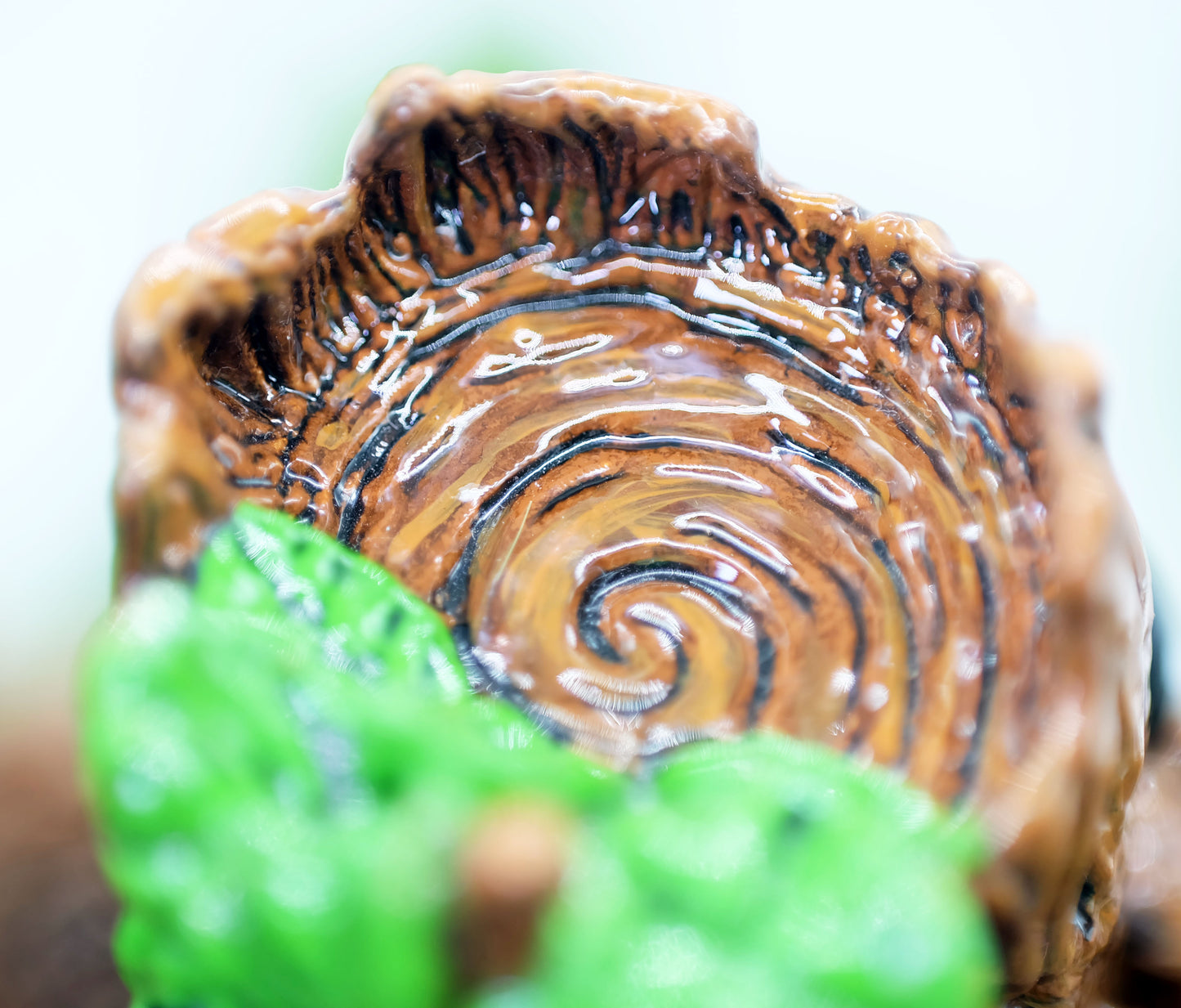 a close up photo showing the detail of the very top of he sculpture's head. This handmade and handpainted sculpture from this angle resembles the rings of a tree, with rough bark around the edges and some leaves coming out to the side